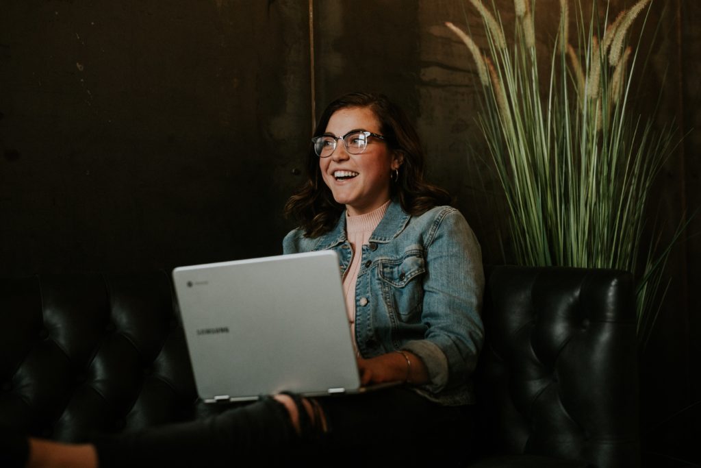 student smiling, sitting, and holding laptop in cafe